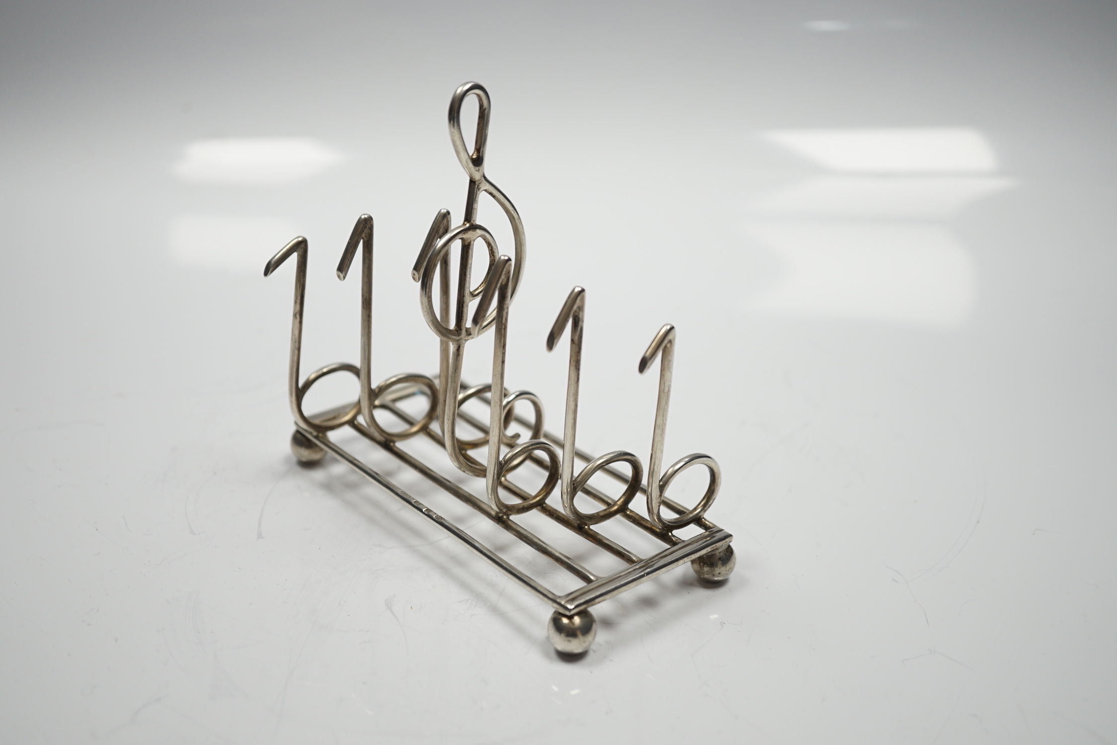 A late Victorian novelty silver toast rack, the dividers modelled as musical notes, with central handle modelled as a treble clef, on ball feet, Norton & White, Birmingham, 1898, length 12.5cm, 139 grams.